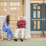 A nurse and an elderly man sitting in two rocking chairs